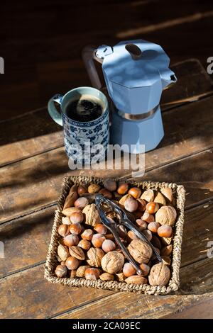 Korb mit Nüssen und heißem Kaffee auf alten, dunklen Holztisch - entspannende Zeit am Nachmittag, während des Aufenthalts zu Hause. Stockfoto