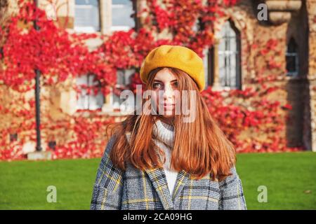 Junge Frau in gelber Baskenmütze am Herbsttag auf dem Hintergrund des Efeu-geflochtenen Gebäudes Stockfoto