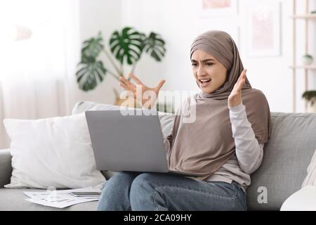Computerprobleme. Wütend arabische Frau mit Problemen mit Laptop zu Hause Stockfoto