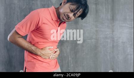 Junge asiatische Mann mit einem Magen Schmerzen auf Zement Wand Hintergrund mit Kopierer Raum, Probleme und Konzepte der Gesundheitsversorgung Stockfoto