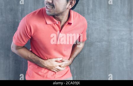 Junge asiatische Mann mit einem Magen Schmerzen auf Zement Wand Hintergrund mit Kopierer Raum, Probleme und Konzepte der Gesundheitsversorgung Stockfoto