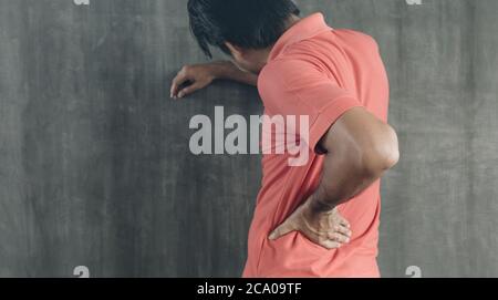 Hand des Mannes, der ihre Rückenschmerzen auf Zementwand-Hintergrund berührt, mit Kopierraum, Problemen und Gesundheitskonzepten Stockfoto