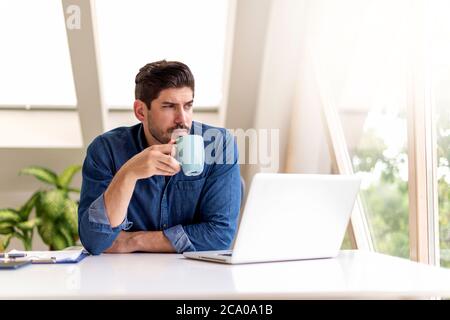 Ein Foto eines unglücklichen Geschäftsmannes, der nachdenklich aussass, während er am Schreibtisch saß und Tee trank. Heimbüro. Stockfoto