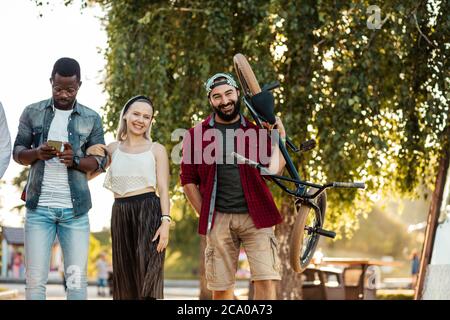 Junger BMX-Fahrer in Gesellschaft mit seinen multiethnischen Freunden zu Fuß, um eine gute Zeit im Stadtpark haben Stockfoto