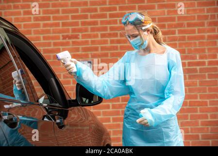Salisbury, England, Großbritannien. 2020. Covid-19 Tester trägt Schutzkleidung, Visier, Maske und Schutzbrille mit Stirnthermometer zur Temperaturkontrolle Stockfoto