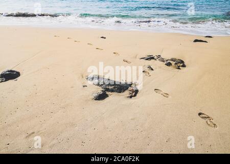 Fußabdrücke von Schuhsohlen an einem einsamen Sandstrand mit der Meeresbrandung, die in Playa Blanca, Lanzarote, Spanien, während der Coronavirus-Krise zu sehen ist. Stockfoto