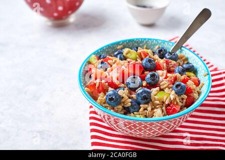 Gesunde Haferflocken mit Früchten und Beeren, Erdbeeren, Heidelbeeren und Feigen in einer blauen Schüssel auf grauem Hintergrund für das Frühstück Stockfoto