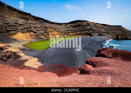 Lago Verde ('Green Lake') in El Golfo, Lanzarote, Kanarische Inseln, Spanien. Bunte Landschaft mit schwarzem Sandstrand, dunklen vulkanischen Felsen und roter Erde. Stockfoto