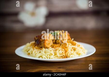 Gekochte Vermicelli mit Fleisch und Gravy auf einem Teller auf einem Holztisch Stockfoto