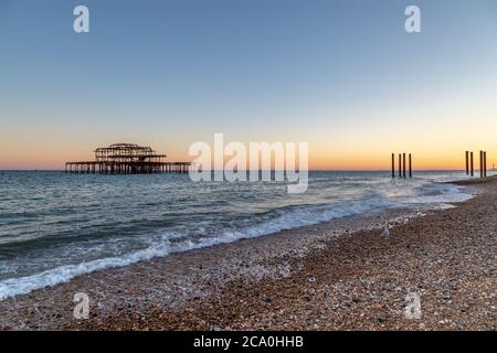 Blick über Brighton Beach in Richtung West Pier, mit einem Sonnenuntergang dahinter Stockfoto