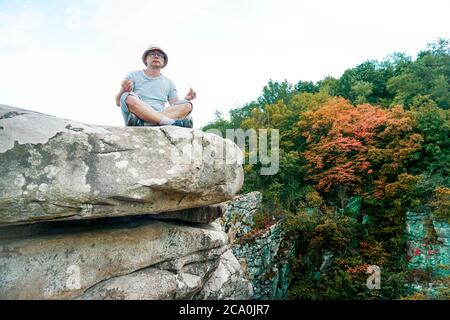 Ein Kerl sitzt auf einem Felsen in den Bergen auf einem Stein, gekleidet in ein T-Shirt und Shorts Stockfoto