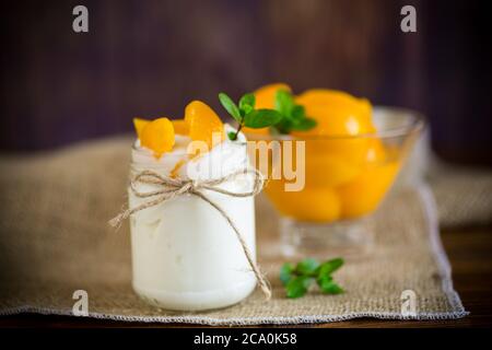 Hausgemachter süßer Joghurt mit eingelegten Pfirsichscheiben in einem Glas auf einem Holztisch Stockfoto