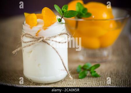 Hausgemachter süßer Joghurt mit eingelegten Pfirsichscheiben in einem Glas auf einem Holztisch Stockfoto