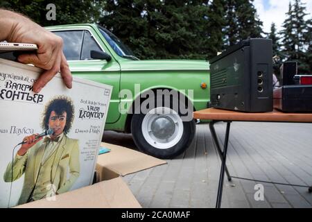 Rjasan, Russland. 1. August 2020 EIN Mann zieht eine Schallplatte mit Aufnahmen von Liedern des sowjetischen Sängers Valery Leontiev vor dem Hintergrund des alten sowjetischen Autos Saparoschets im Central Park der Stadt Rjasan, Russland Stockfoto