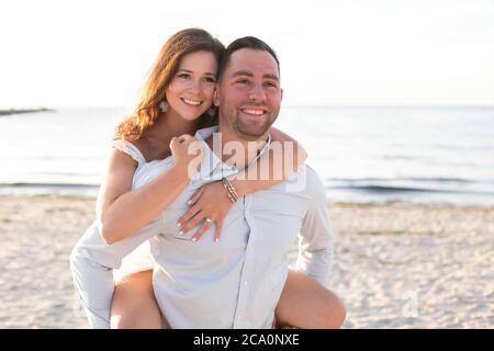 Mann, der Frau auf dem Rücken am Strand lächelnd trägt Stockfoto