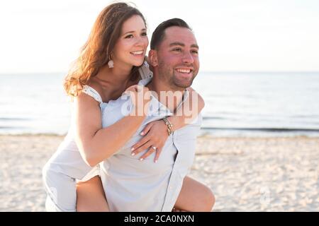 Mann, der Frau auf dem Rücken am Strand lachend trägt Stockfoto