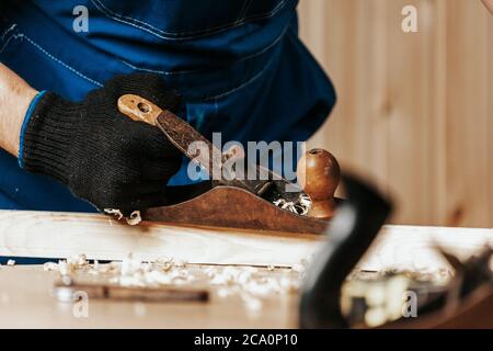 Nahaufnahme der ein junger Mann Baumeister in der Arbeit Klumpen und schwarze Handschuhe Griffe eine Holzstange mit einem Wagenheber Flugzeug in der Werkstatt, im Hintergrund ein l Stockfoto