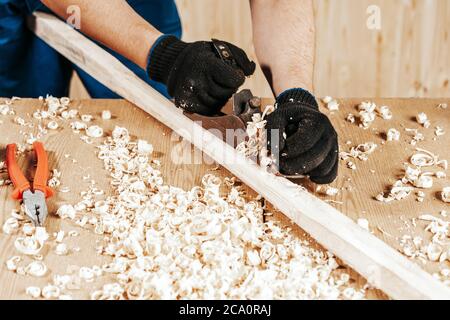 Nahaufnahme der ein junger Mann Baumeister in Arbeit Klumpen und schwarze Handschuhe Griffe eine Holzstange mit einem Wagenheber Flugzeug in der Werkstatt Stockfoto