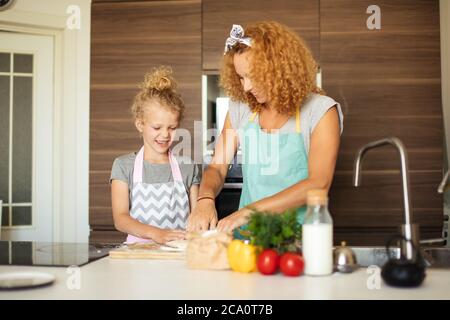 Fröhliche weibliche Köchin backt leckeren Apfelkuchen für besondere Anlässe, zeigt ihr Kochtalent zu ihrem sechsjährigen Mädchen in der modernen Hausküche. Stockfoto