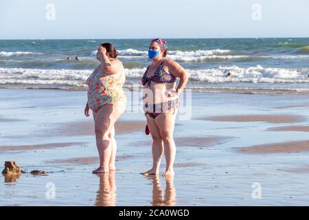 Punta Umbria, Huelva, Spanien - 2. August 2020: Zwei übergewichtige Frauen am Strand tragen schützende oder medizinische Gesichtsmasken. Neue Normalität in Spanien mit SoC Stockfoto