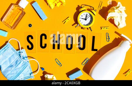 Text SCHULE auf gelbem Hintergrund mit Schulbedarf, Schutzmaske und Desinfektionsmittel antiseptisch. Zurück zur Schule. Neuer Normalwert. Schulquarantäne Stockfoto