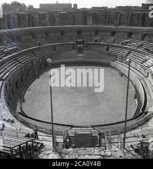 1960, historische Ansicht aus dieser Zeit des antiken römischen Amphitheaters in Arles, Südfrankreich mit Blick auf die ovale Arena. Um 90 n. Chr. erbaut, um Unterhaltung in Form von Chariot-Rennen und Hand-an-Hand-Schlachten der Gladiatoren bieten, wurde es später ein Unterschlupf für Peop und eine Festung. Im 19. Jahrhundert wurden die Gebäude innerhalb der Arena niedergeschlagen und sie wurde wieder einmal ein Ort der Unterhaltung, wo Stierkämpfe und Konzerte veranstaltet wurden. Ein Amphitheater leitet sich von dem anicent griechischen Wort meaing 'Ort für die Betrachtung'. Stockfoto