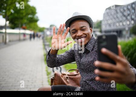 Schwarzer Mann Pendler sitzen auf Bank im Freien in der Stadt, Videoanruf Konzept. Stockfoto