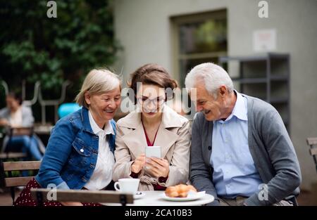 Frau mit älteren Eltern sitzen im Café, mit Smartphone. Stockfoto