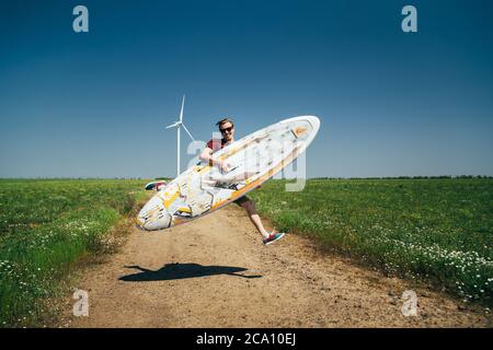 ODESSA, UKRAINE - MAI, 20 2015: Der junge Hipster-Surfer, der mit einem alten Surfbrett springt, ist auf dem Weg zum Strand Stockfoto
