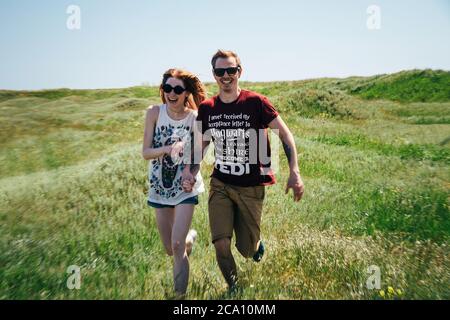 ODESSA, UKRAINE - MAI, 20 2015: Nettes junges Hipster-Paar läuft mitten im grünen Feld. Guten Tag, Glück, Freundschaft, Spaziergang, Urlaub Stockfoto