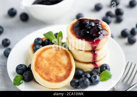 Quark-Fritten mit Heidelbeermarmelade auf weißem Teller. Russische, ukrainische Küche. Süße Syrniki, gebratene Käsepfannkuchen Stockfoto