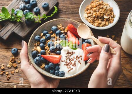 Essen Müsli mit griechischem Joghurt und Beeren. Weibliche Hände halten Schüssel mit gesunden Frühstücksflocken Müsli mit Obst und Joghurt. Konzept der Reinigung Stockfoto