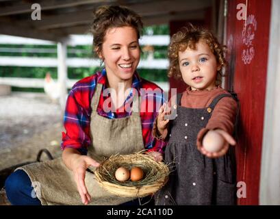 Portrait der Mutter mit kleiner Tochter auf dem Bauernhof stehend, mit Korb mit Eiern. Stockfoto