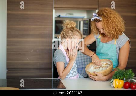 Fröhliche weibliche Köchin backt leckeren Apfelkuchen für besondere Anlässe, zeigt ihr Kochtalent zu ihrem sechsjährigen Mädchen in der modernen Hausküche. Stockfoto