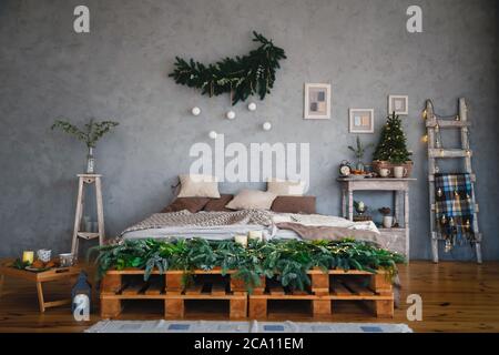 Zimmer im Loft-Stil mit modernem Design und einem Doppelbett in hellen Farben, das für die Weihnachts- und Winterferien eingerichtet ist. Weihnachten und Neujahr Konzept Stockfoto