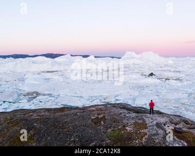 Reisen Sie in arktische Landschaft Natur mit Eisbergen - Grönland Tourist Explorer. Person, die auf den erstaunlichen Grönland eisfjord schaut - Luftbild. Mann durch Eis Stockfoto