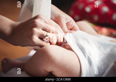 Nahaufnahme der Füße des Babys in den Händen der Mutter. Mutter wechselt die Kleidung des Babys. Taufe in der orthodoxen christlichen Kirche Stockfoto