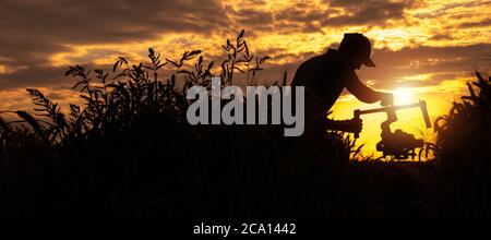 Videooperator mit moderner Kamera, installiert auf einem Gimbal, der während des szenischen Sonnenuntergangs durch die Landschaft läuft. Panorama Silhouette Konzept. Stockfoto