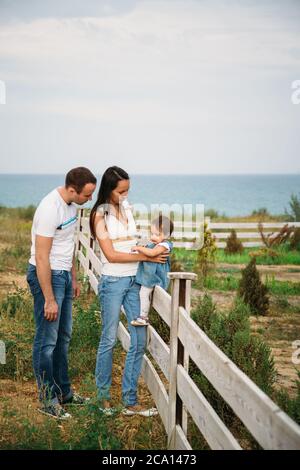 Nahaufnahme von kleinen Mädchen in blauen Jeans Kleid sitzt auf einem Zaun mit Mutter und Vater in der Nähe Stockfoto