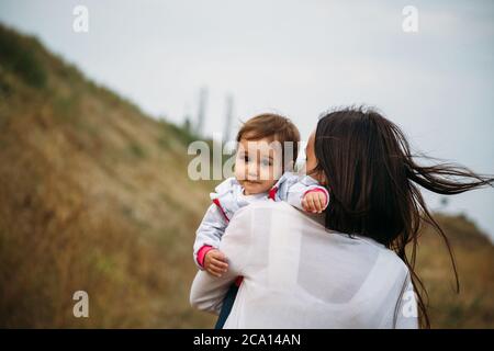 Glückliche junge Mutter mit einer kleinen Tochter in den Händen, im Freien Hintergrund Stockfoto