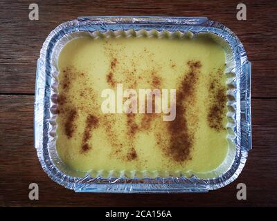 Canjica Curau. Typische brasilianische Junina Party Süßigkeiten. Rustikaler Holzhintergrund. Brasilianisches Dessert. Nahaufnahme. Draufsicht. Aluminiumbehälter Stockfoto