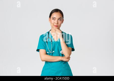 Covid-19, Mitarbeiter im Gesundheitswesen, Pandemiekonzept. Nachdenklich smart asiatische Krankenschwester in Scrubs wegschauen und denken, lächelnd zufrieden. Arzt haben Stockfoto