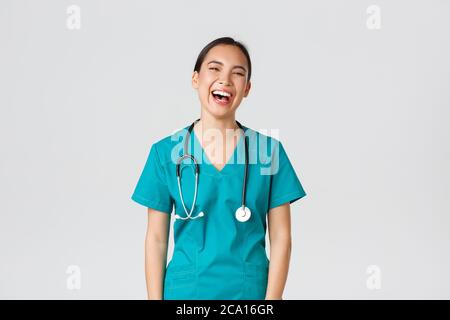 Covid-19, Mitarbeiter im Gesundheitswesen, Pandemiekonzept. Sorglos schöne weibliche asiatische Krankenschwester in Scrubs, Praktikant Spaß haben, lachen glücklich. Arzt beim Mittagessen Stockfoto