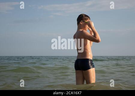 Ein 10-jähriger Junge zieht eine Schwimmbrille an und bereitet sich auf das Schwimmen im Meer vor. Stockfoto