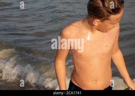 Ein gutaussehender Junge 10 Jahre alt kommt bei Sonnenuntergang aus dem Wasser an der Küste. Stockfoto
