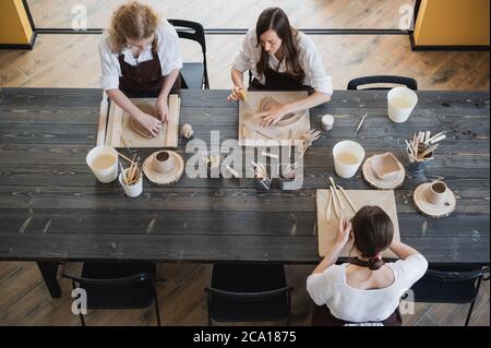 Draufsicht auf weibliche Töpfer während des Arbeitsprozesses in der Tonwerkstatt. Frau Meister bereiten Keramik-und Ton-Produkte an großen Holztisch Stockfoto