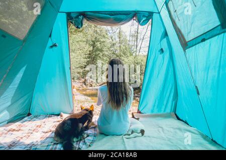 Weibliche Reisende im Camp in einem Wald mit ihren Hunden zusammen auf einer Naturreise, Freundschaftskonzept, Outdoor-Aktivitäten, Reisen mit einem Haustier. Stockfoto