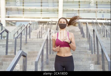 Während des Ausbruchs sicher ausgeführt werden. Junge athletische Frau in Sportkleidung trägt schützende Gesichtsmaske läuft unten in der Stadt während Coronavirus Pandemie. Covid 19 und körperliche Aktivität, Sport Stockfoto
