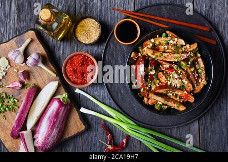 Gaji Namul, gedünstete und gewürzte Aubergine in einer schwarzen Schüssel auf einem Holztisch mit Sojasauce und Essstäbchen und Zutaten auf einem Schneidebrett, koreanische s Stockfoto