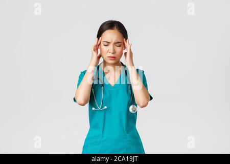 Covid-19, Mitarbeiter im Gesundheitswesen, Pandemiekonzept. Überfordert und müde junge asiatische Krankenschwester Augen schließen, Grimacing von Kopfschmerzen, schwindlig fühlen, Nacht Stockfoto